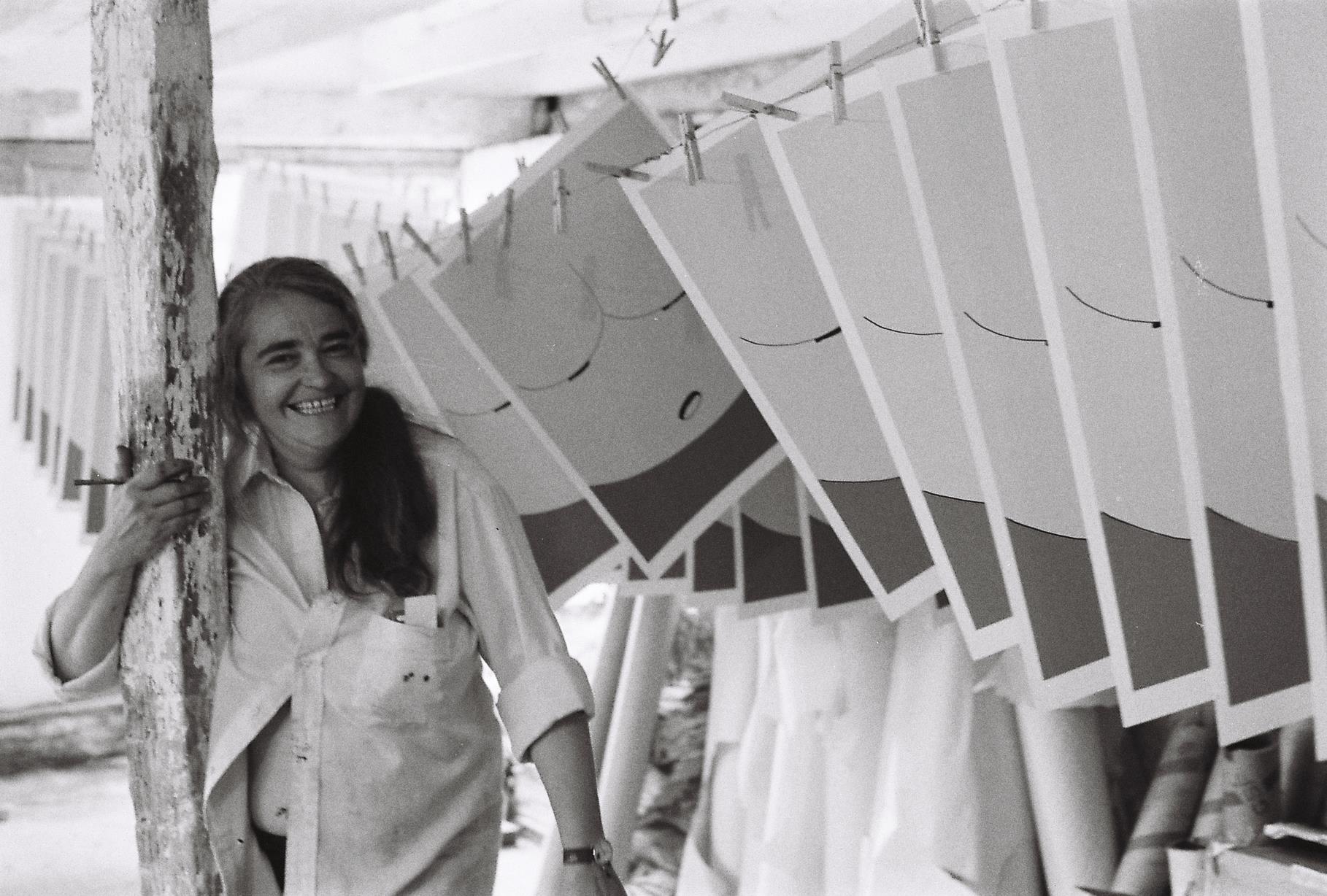 black and white photo of woman showing bellybutton smiling with drying screenprints hang in the foreground